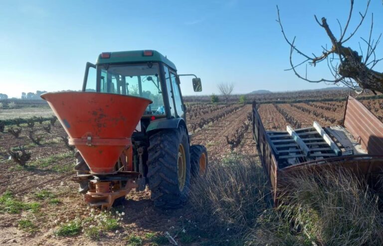 Es una imagen de un tractor abonando en un campo de viña